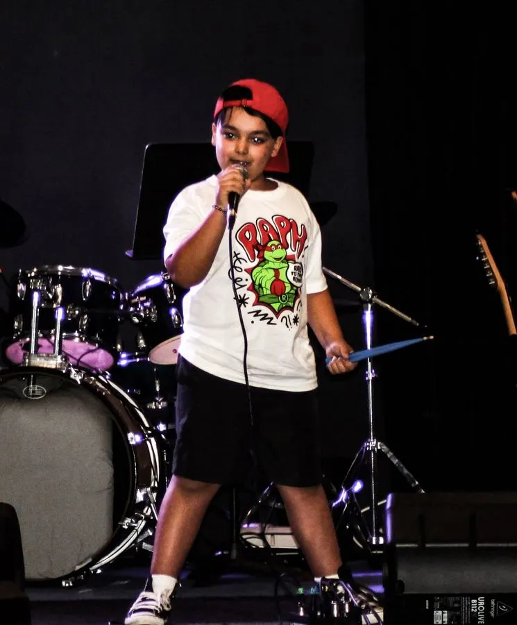 Young boy singing into a microphone on stage in front of a drum kit